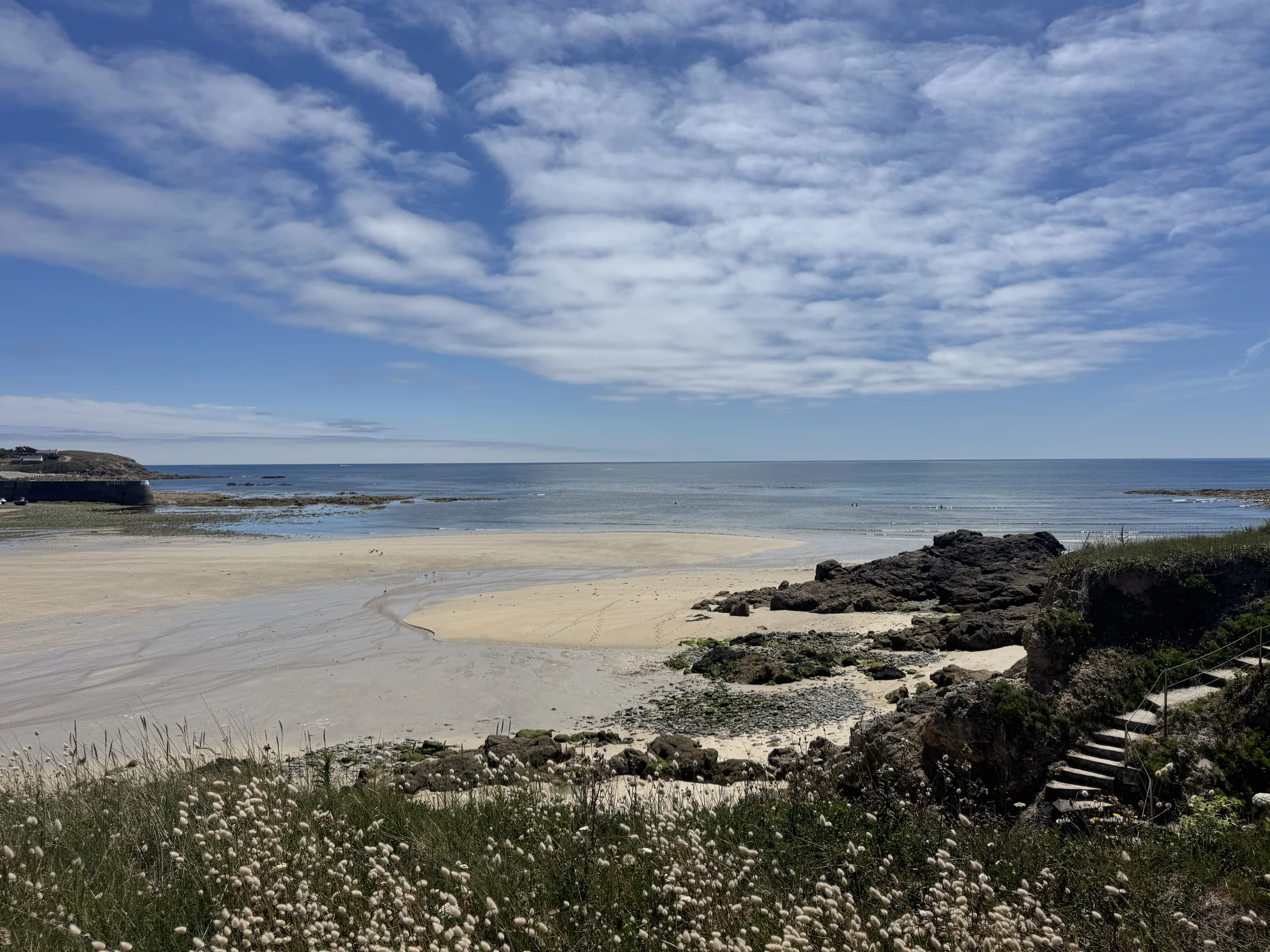 Heller Sandstrand mit Felsen, blauem Meer und weitem Wolkenhimmel
