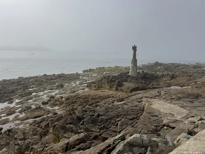 Ein Leuchtturm ragt aus einer rauen Felslandschaft unter einem hellgrauen Himmel.