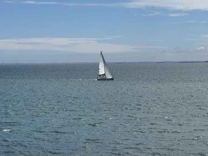 Ein weißes Segelboot hebt sich von der weiten, ruhigen blauen Wasserfläche ab.