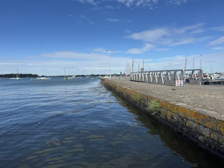 Eine lange steinerne Mole führt hinaus ins blaue Wasser unter einem weit geöffneten Himmel.