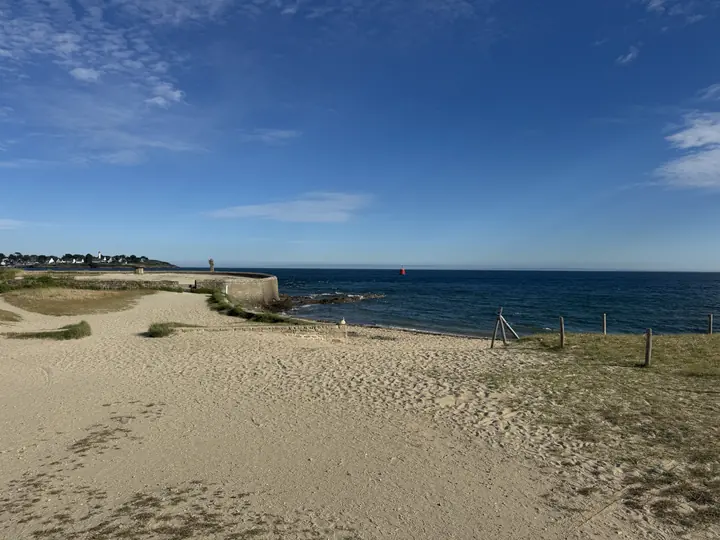 Heller Sand und niedrige Dünen öffnen den Blick auf das blaue Meer.