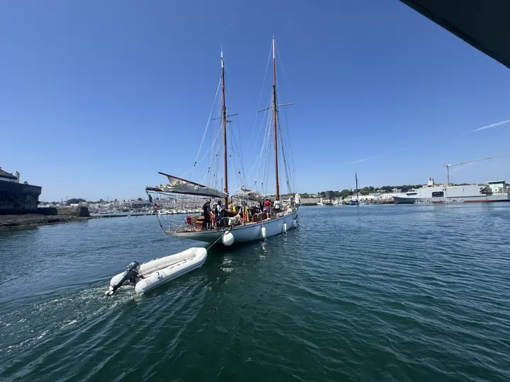 Ein traditionelles Segelschiff liegt auf türkisblauem Wasser vor den Häusern am Hafen.